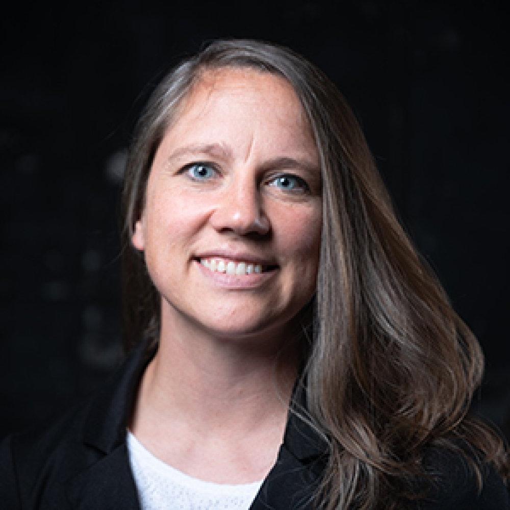 Lady with long dark hair wearing black cardigan and white top in front of dark background